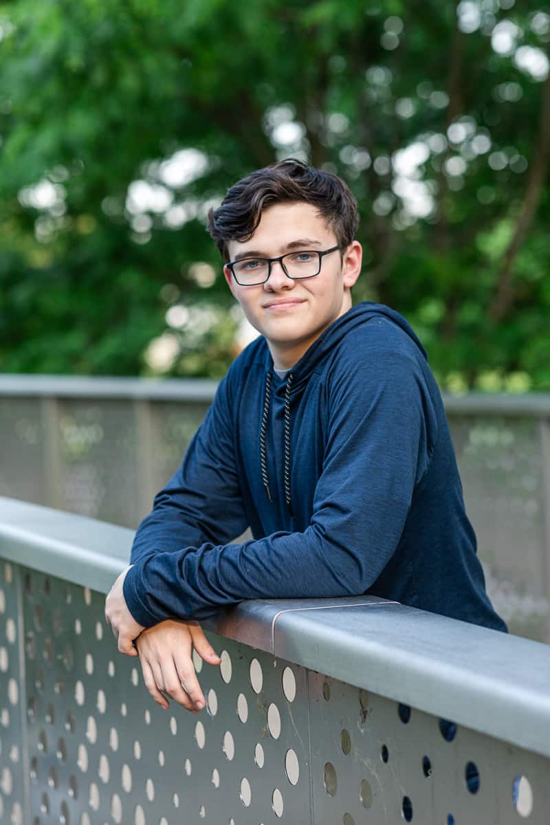 senior boy in navy hoodie leaning over bridge railing